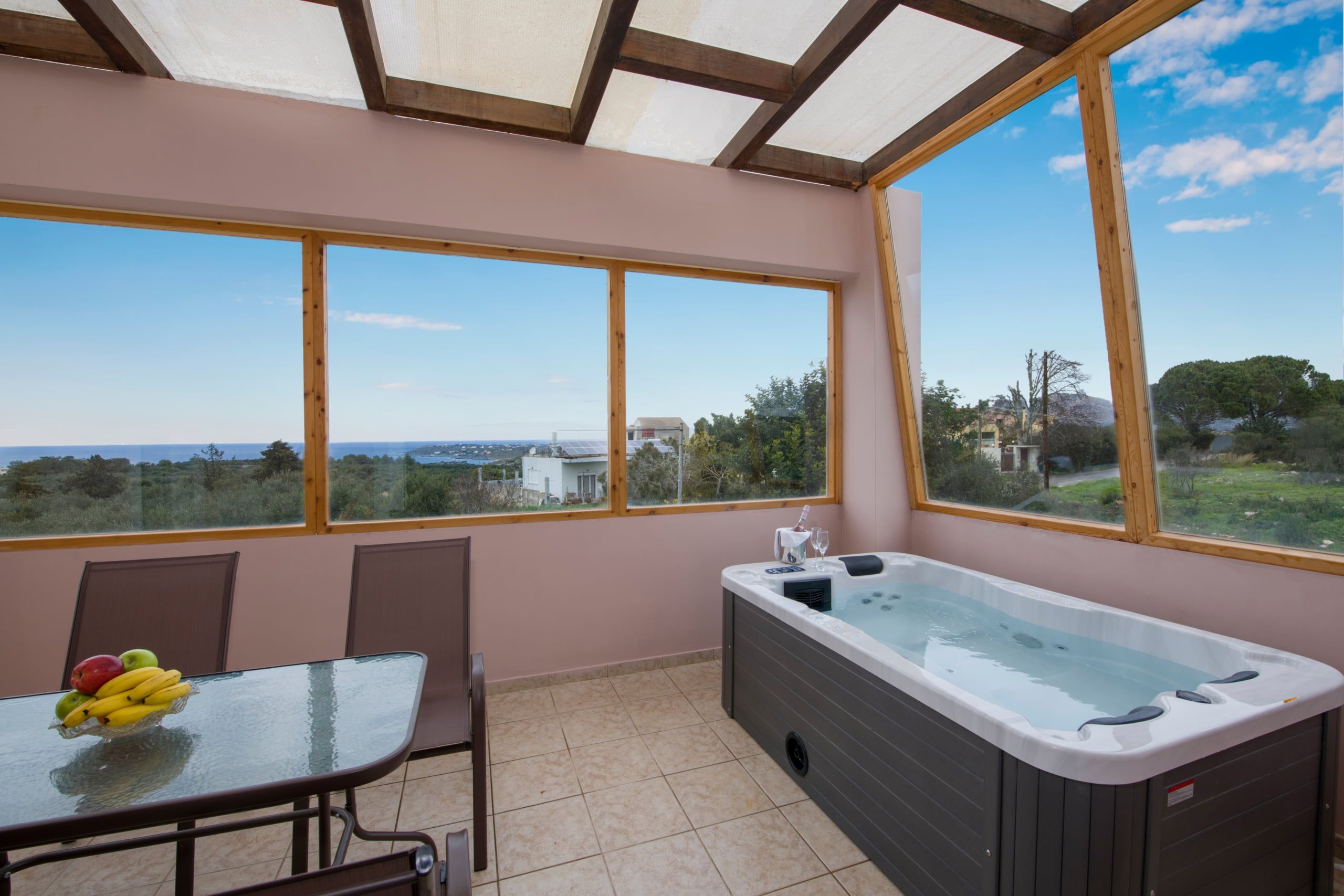 A room with a hot tub, a table with fruit, and large windows offering a view of the landscape.