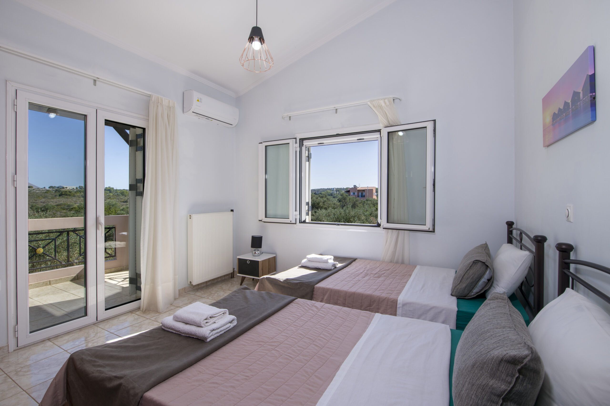 Habitación de hotel con dos camas, vistas al exterior, un radiador y una lámpara en el techo.