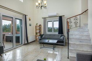 A spacious living area with a sofa, a coffee table, a staircase, and a view of the outdoors. - Villa Ifigeneia with Indoor Hot Tubs (Chania)