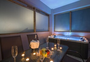 Ein Zimmer mit Whirlpool, einem Tisch mit Kerzen und einer Champagnerflasche.