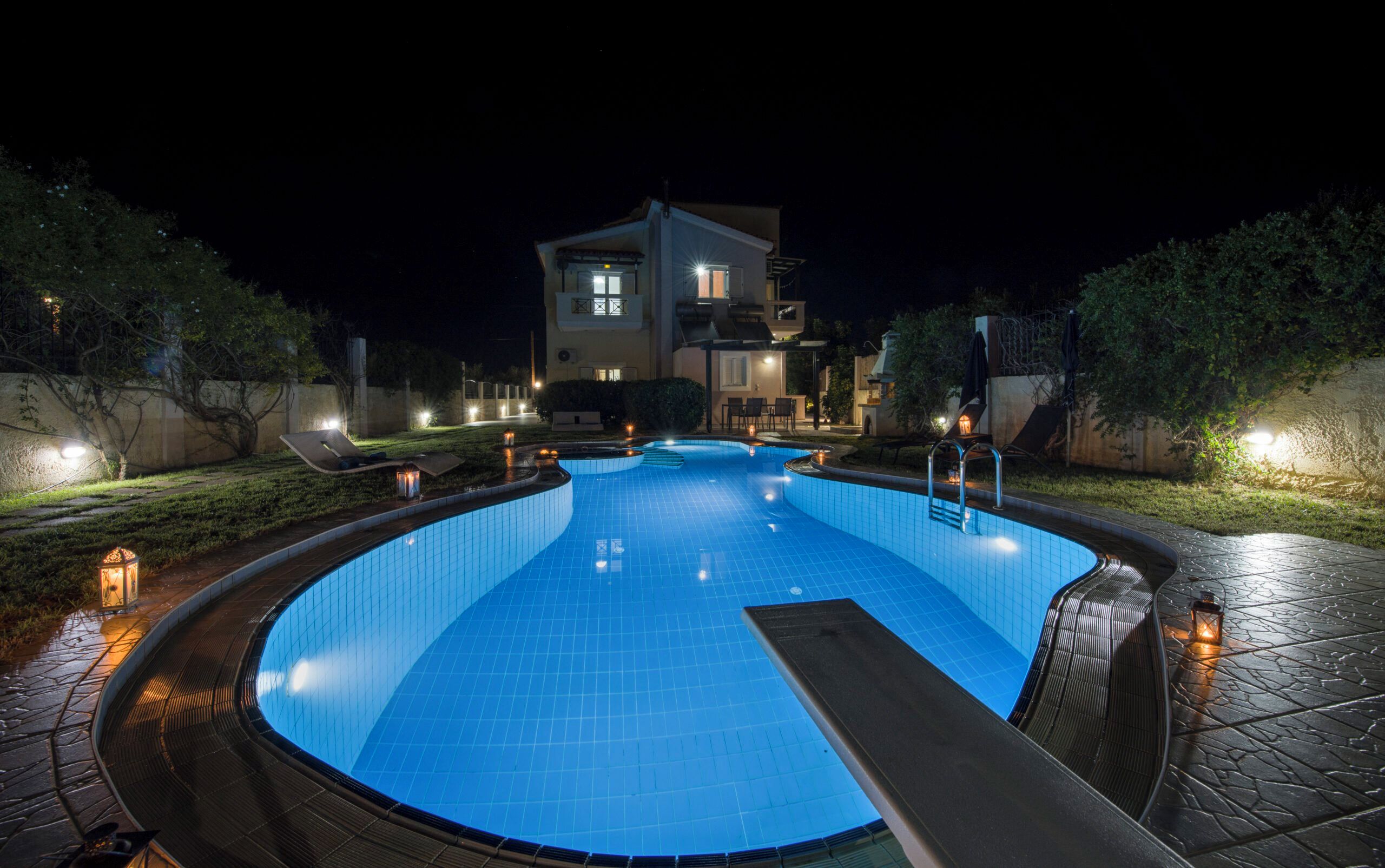 A swimming pool with a curved edge, surrounded by a stone deck, and a building with multiple balconies in the background.