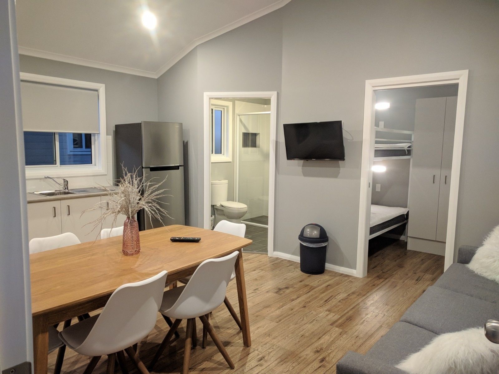 A compact living space with a kitchenette, a dining area, a sofa, and a TV mounted on the wall.
