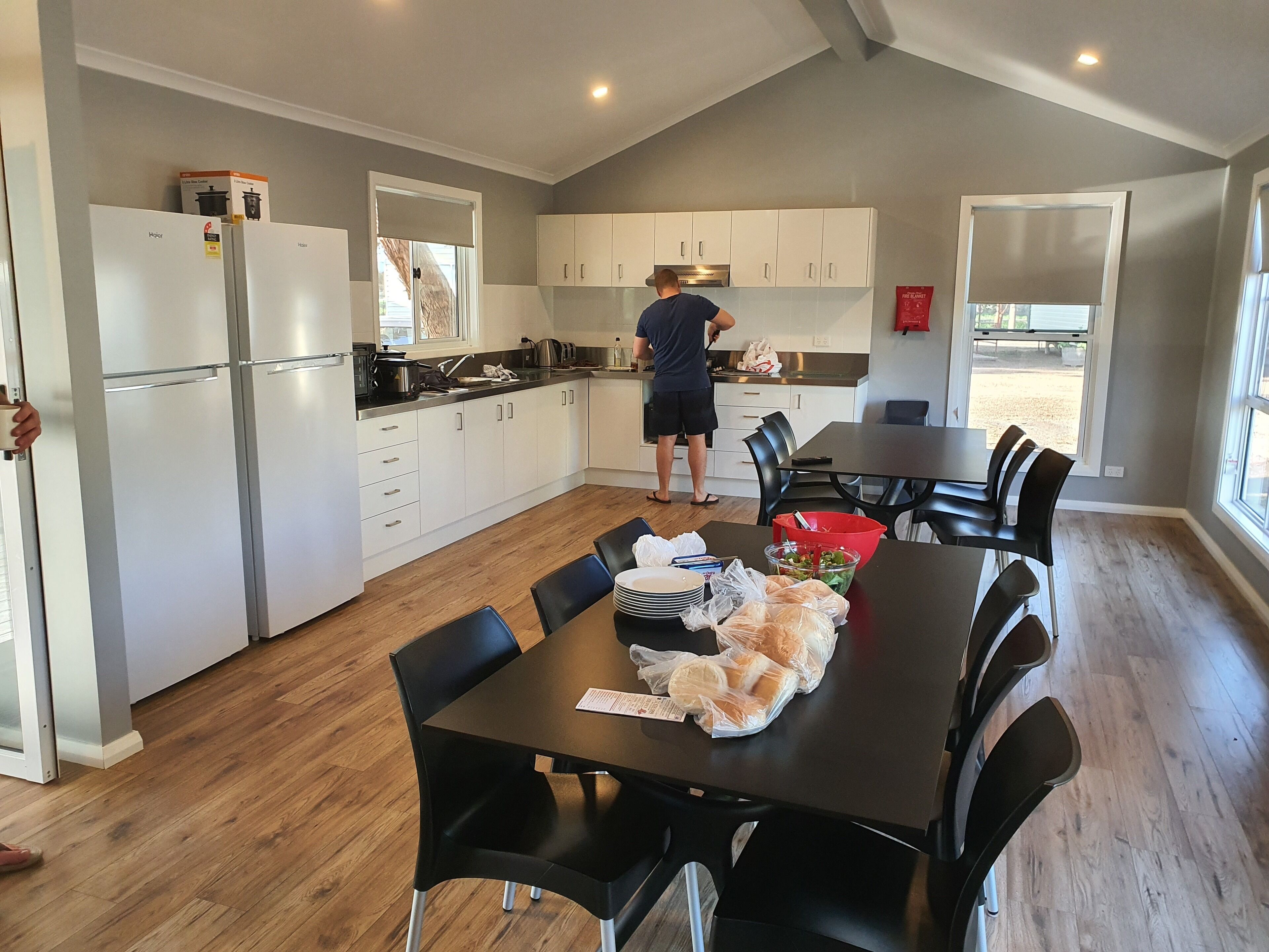 A modern kitchen with white cabinets, a dining area with a table and chairs, and a person cooking at the counter.
