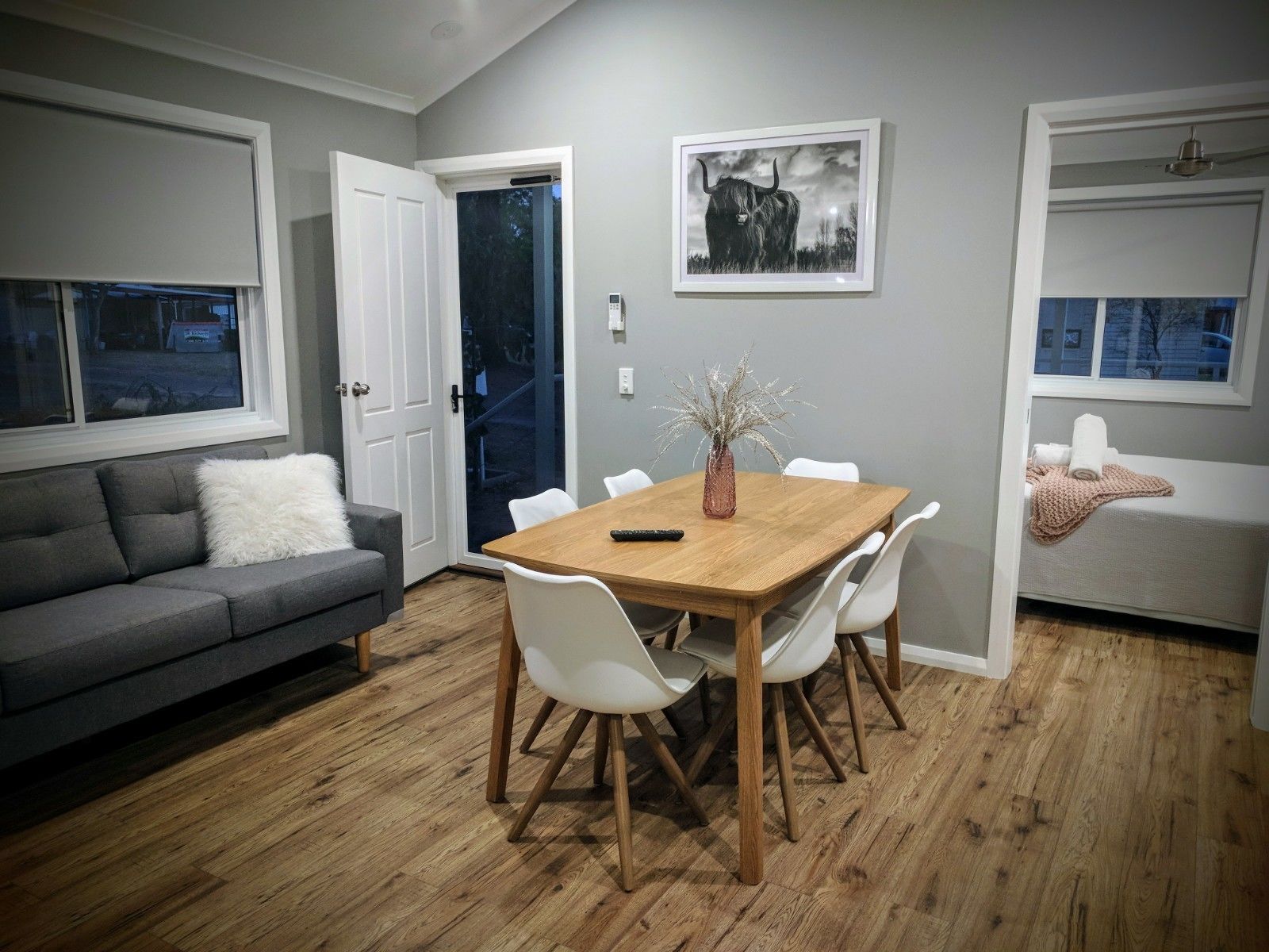 Un comedor con una mesa de madera, sillas blancas, un sofá gris y un banco blanco.