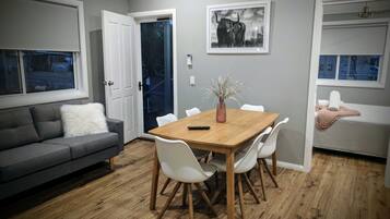 Un comedor con una mesa de madera, sillas blancas, un sofá gris y un banco blanco.
