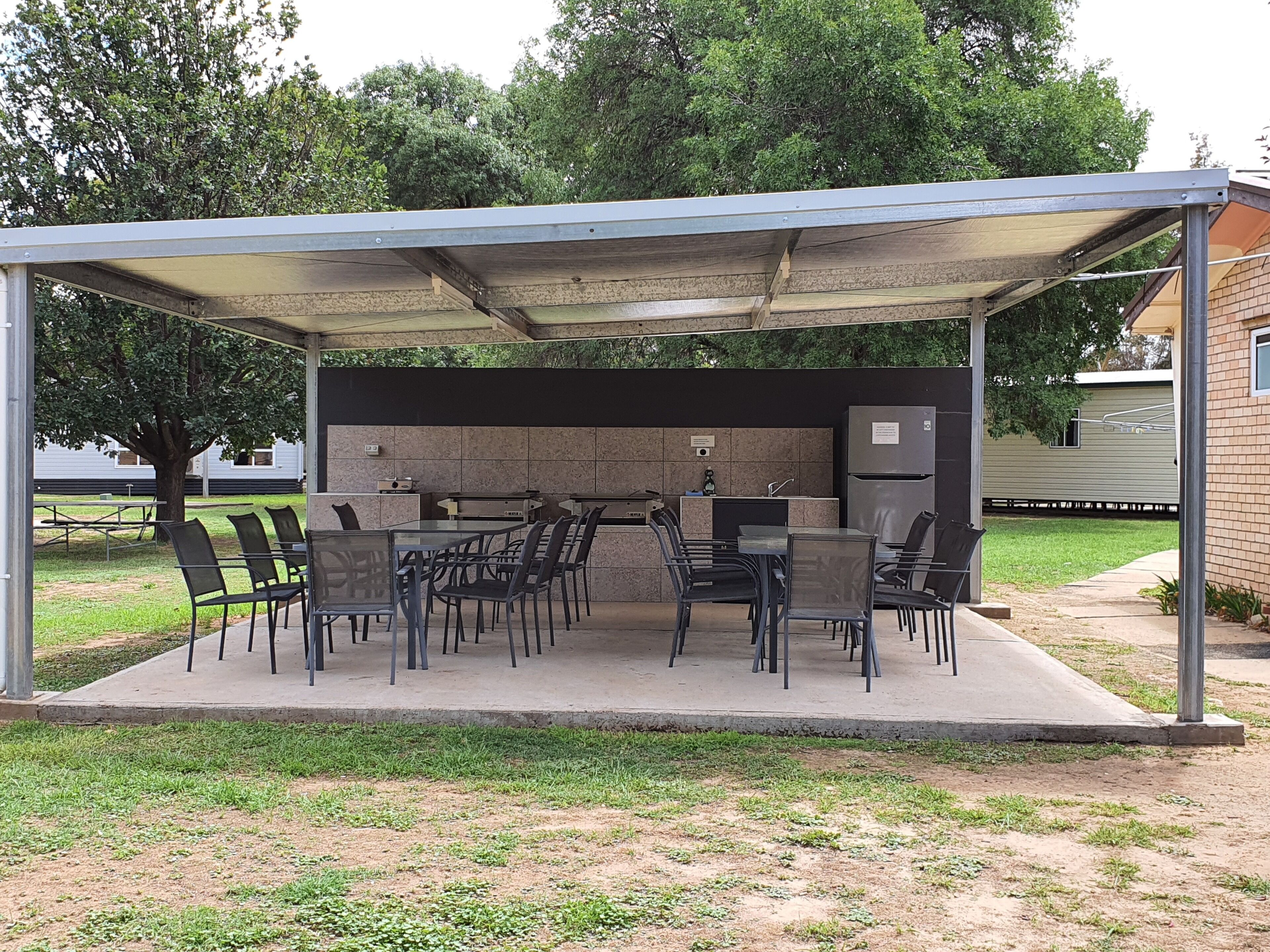 Um pátio externo com mesas e cadeiras, uma pequena área de cozinha e um espaço de estar coberto.