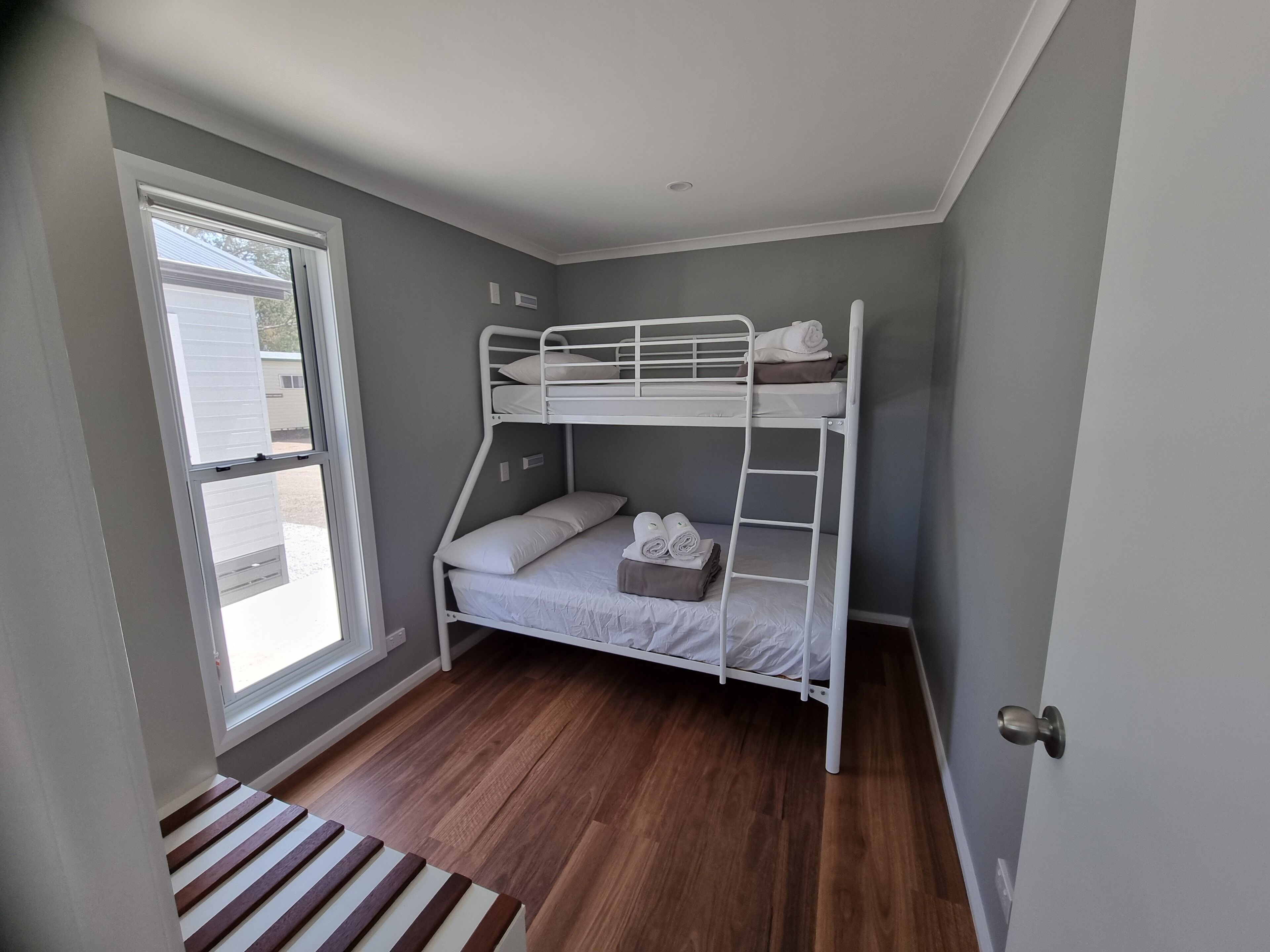 A bunk bed room with a window, wooden flooring, and a door.