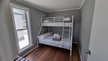 A bunk bed room with a window, wooden flooring, and a door.