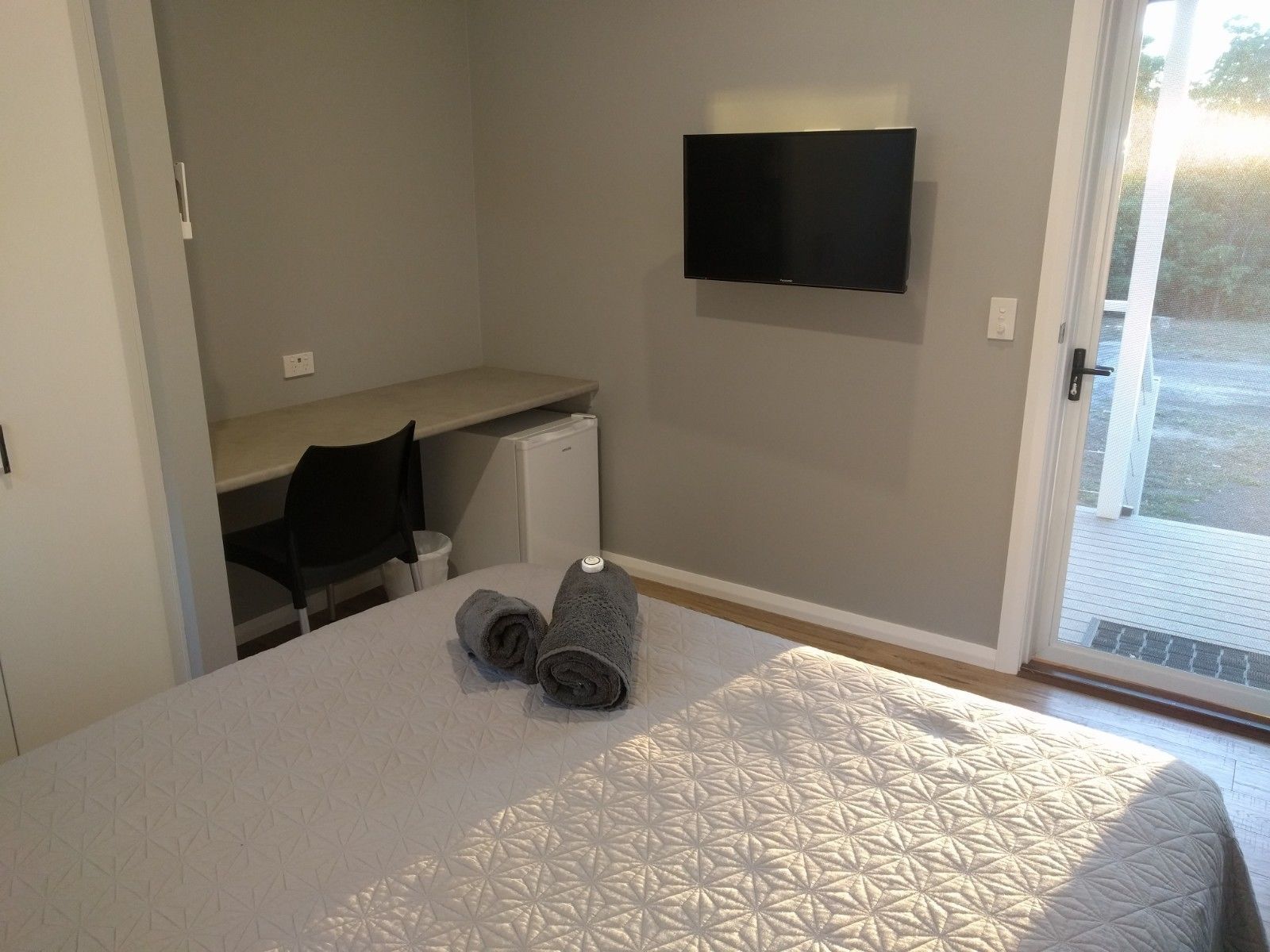 A bedroom with a bed, a desk, a chair, a TV, and a window.