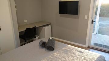 A bedroom with a bed, a desk, a chair, a TV, and a window.
