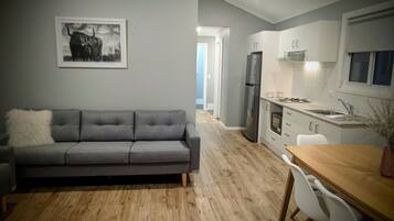 A modern kitchen with a grey sofa, wooden flooring, and a dining table with chairs.