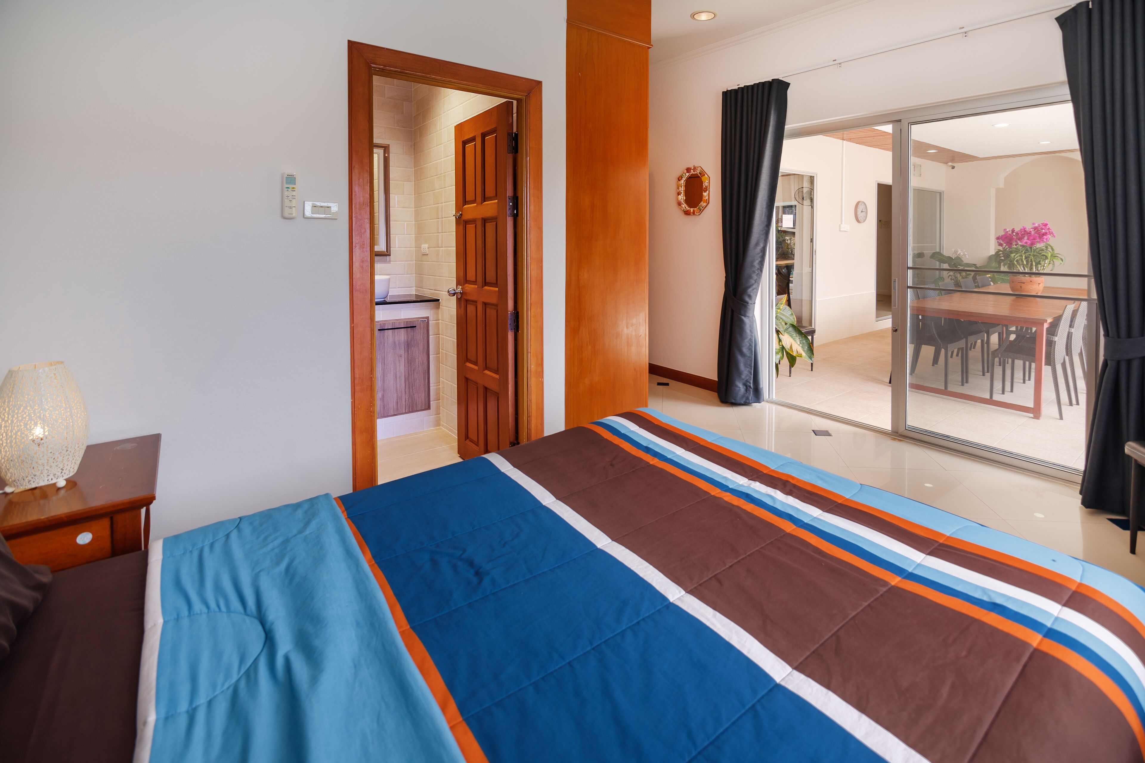 A hotel room with a bed, a nightstand, a lamp, a sliding glass door to a balcony, and a view of the dining area.