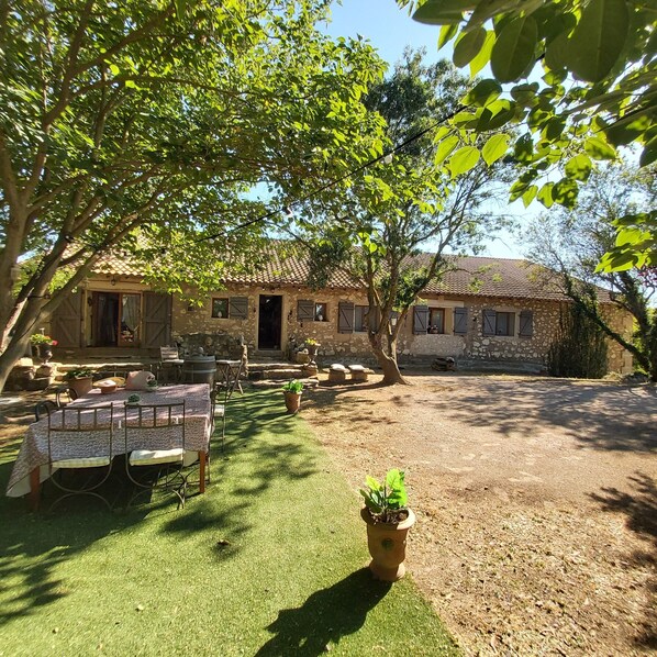 A rustic stone building with a tiled roof, surrounded by a well-maintained lawn and potted plants.