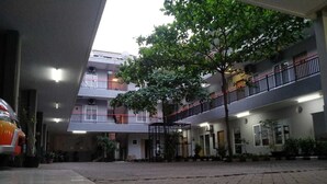A courtyard with a tiled floor, a tree, and a building with balconies. - Hotel Sonic Airport Semarang (Semarang)