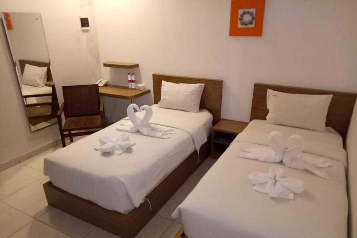 Habitación de hotel con dos camas, una silla, un escritorio con teléfono y una mesita con una botella.
