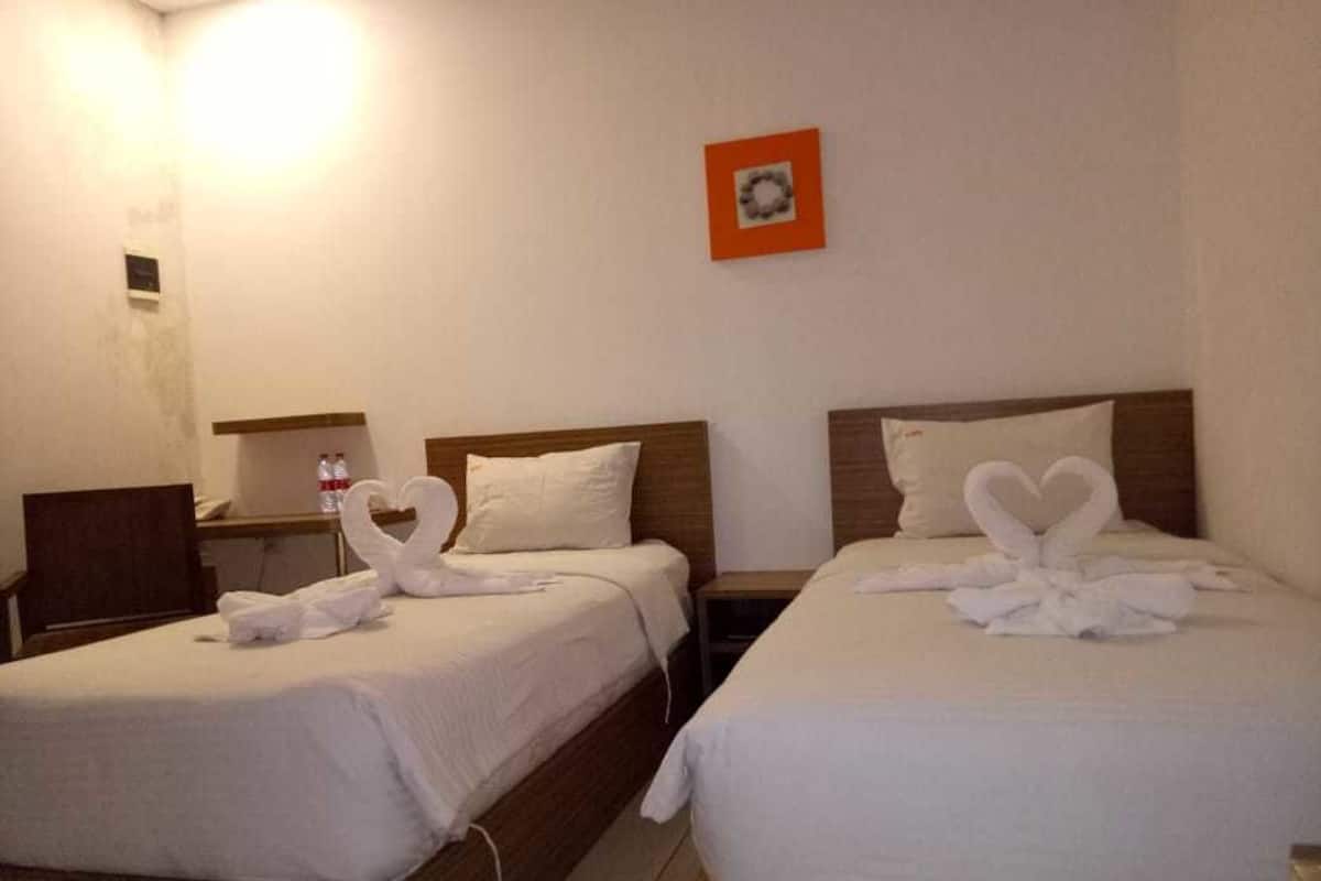 Dos camas individuales con ropa de cama blanca y toallas con forma de corazón, una mesita pequeña y un cuadro colgado en la pared.