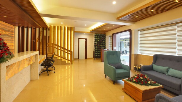 A reception area with a marble counter, a green armchair, a sofa, and a wooden coffee table with flowers. - Park Residency (Kanayannur)