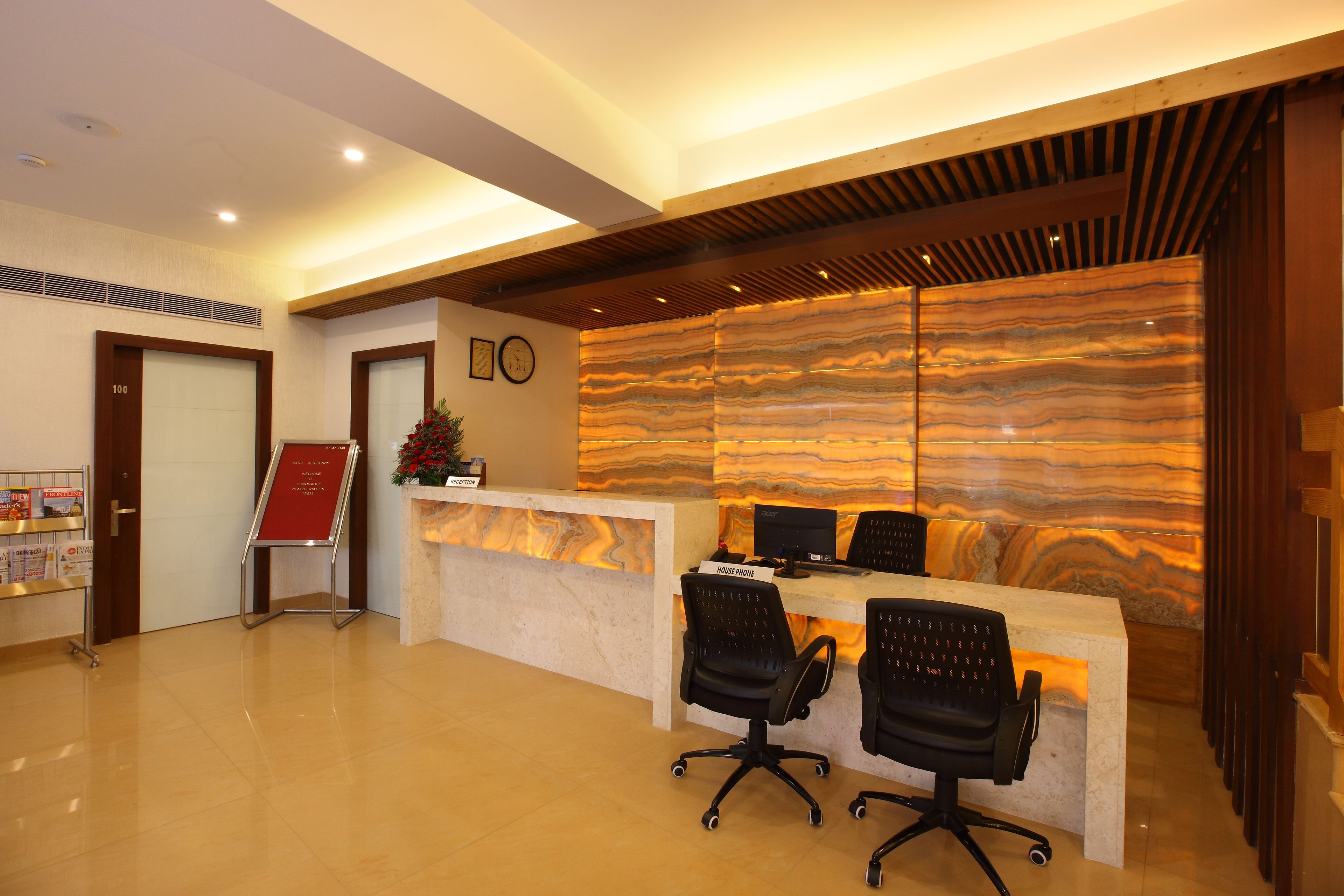 A reception area with a marble counter, two black office chairs, a clock, and a reception desk.