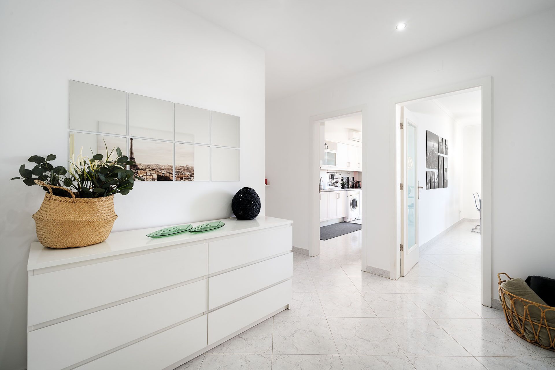 A modern, minimalist hallway with a white console table, a potted plant, and a view of the city through a window.