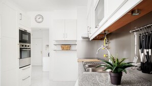 Una cuina moderna amb armaris blancs, forn integrat, una aixeta i una planta en test a la superfície.