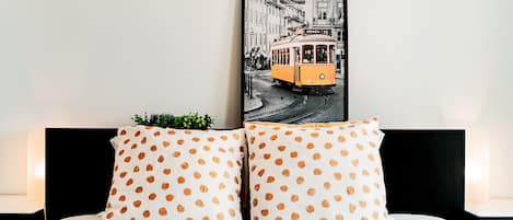 A bed with white bedding and two pillows with a polka dot pattern. A framed picture of a tram is mounted above the bed.