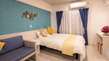 A hotel room with a bed, a nightstand, a blue sofa, a decorative wall piece, a potted plant, and a window with blue curtains.