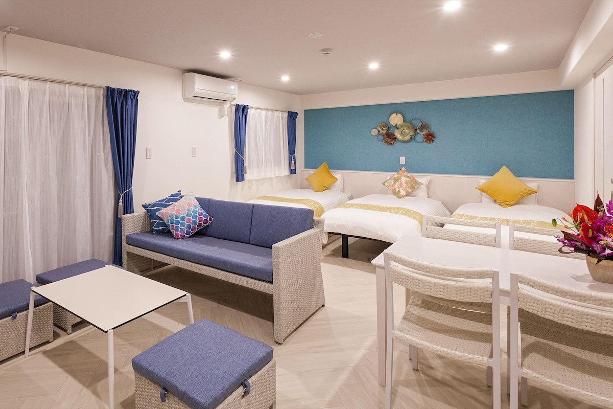 Ein modernes Hotelzimmer mit Sofa, zwei Betten, einem Esstisch und einem kleinen Balkon.