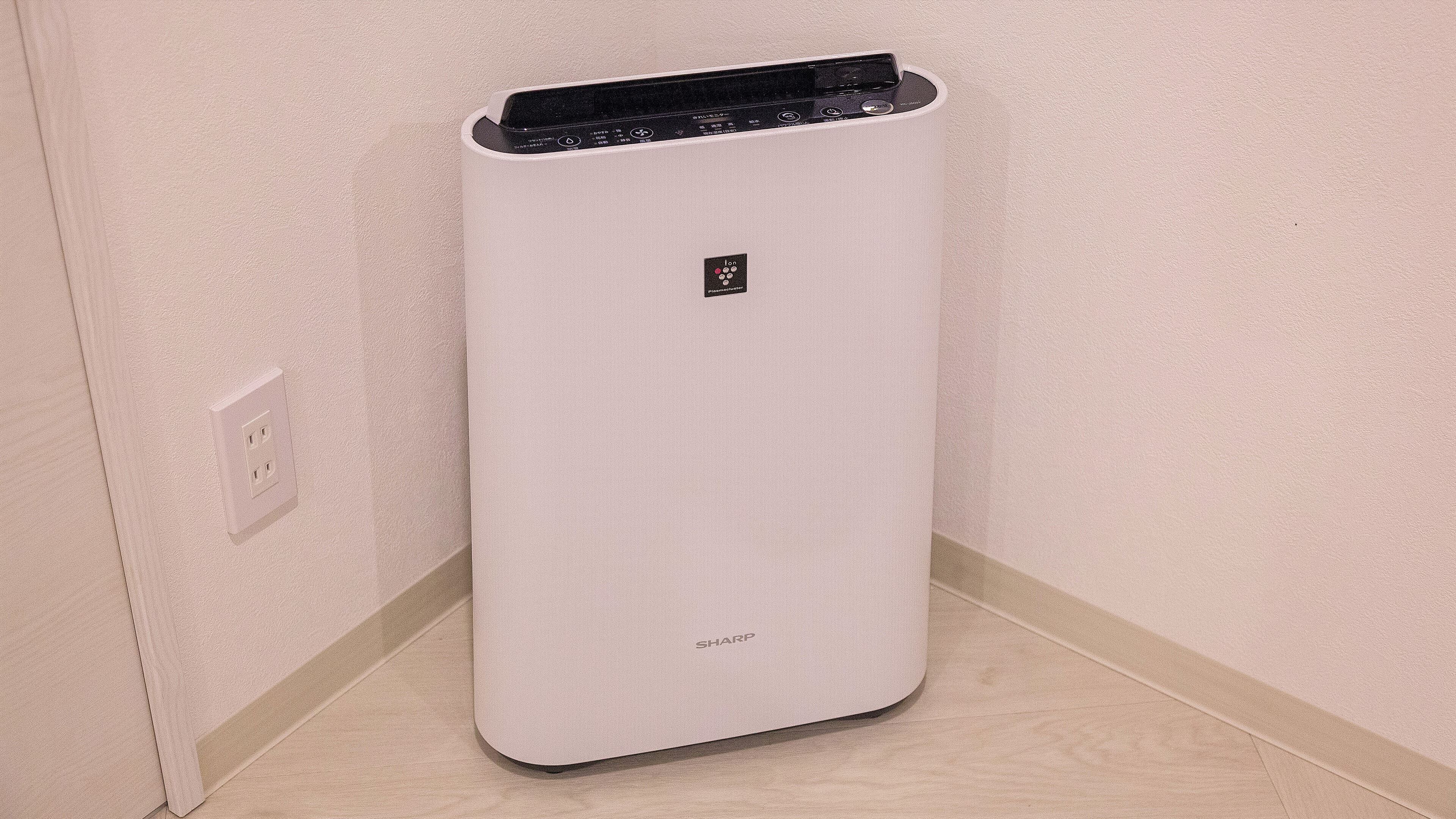 A white, modern, rectangular device with a small logo and the word "SHARP" on it, placed against a light-colored wall with a power outlet nearby.