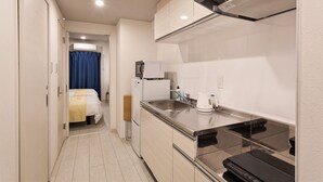 A compact hotel room with a kitchenette, a bed with a blue curtain, and a small bathroom. - Kariyushi Condominium Resort Miyakojima Fukugistays (Miyakojima)
