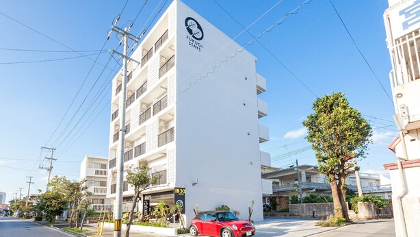 A building with a sign for 'Fukugi Stays' and a red car parked in front. - Kariyushi Condominium Resort Miyakojima Fukugistays (Miyakojima)