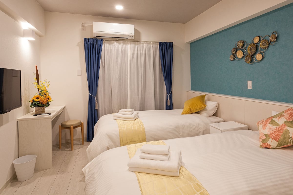 Ein Hotelzimmer mit zwei Betten, einem Schreibtisch mit Stuhl, einem Fernseher und einer Wandklimaanlage.