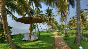 A pathway lined with palm trees leading to a beach, with a thatched umbrella and a seating area. - Shady Shores (Kanayannur)