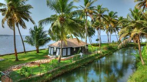 A riverside property with a small building, palm trees, and a view of the water. - Shady Shores (Kanayannur)