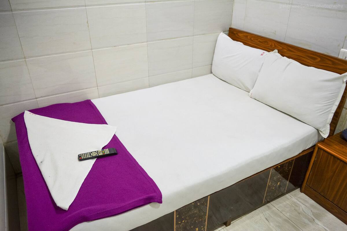 Ein Einzelbett mit weißer Bettwäsche, einer violetten Decke und einer Fernbedienung darauf.