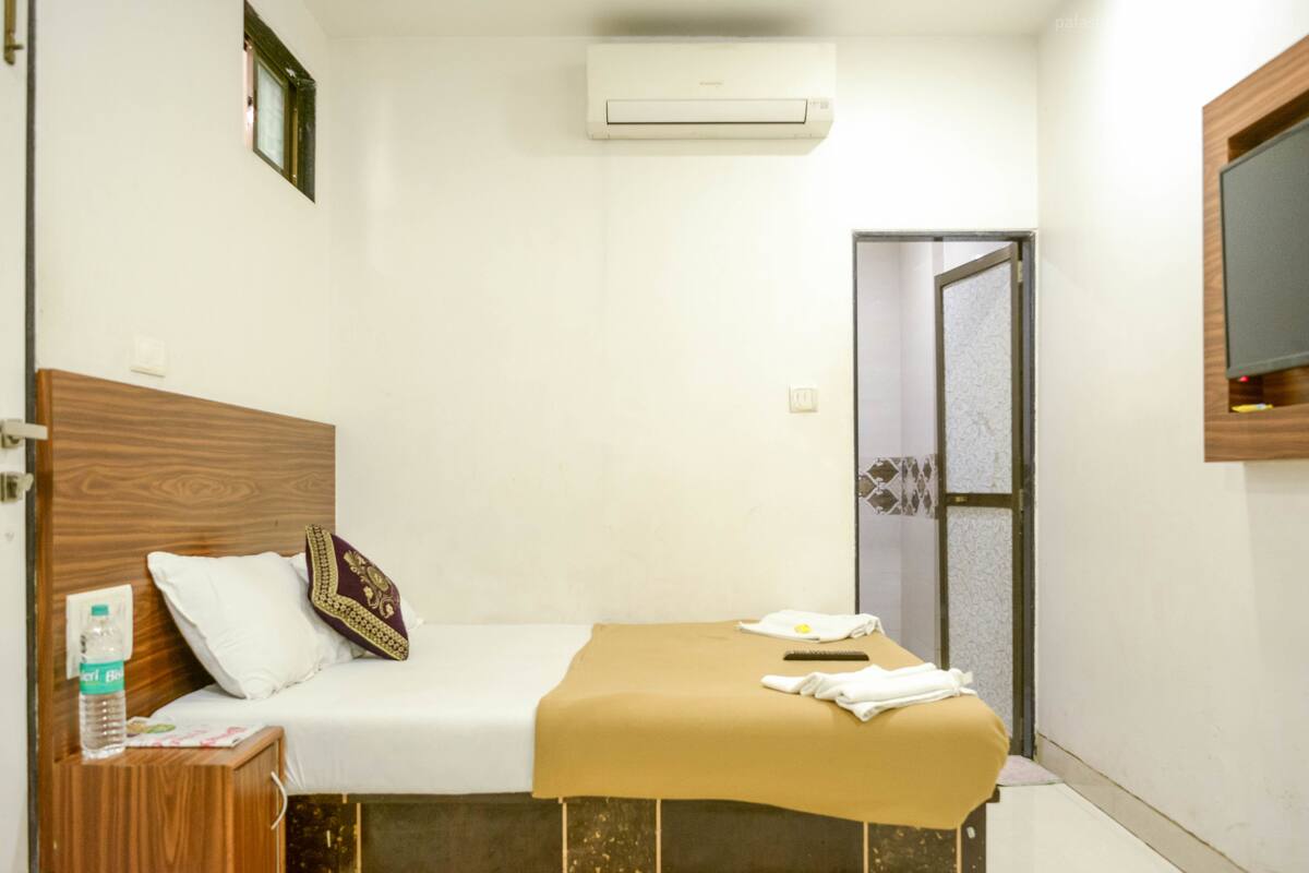 Ein Hotelzimmer mit einem Bett, einem Holz-Kopfteil, einem Nachttisch mit einer Wasserflasche, einem Handtuch und einem kleinen Beistelltisch.