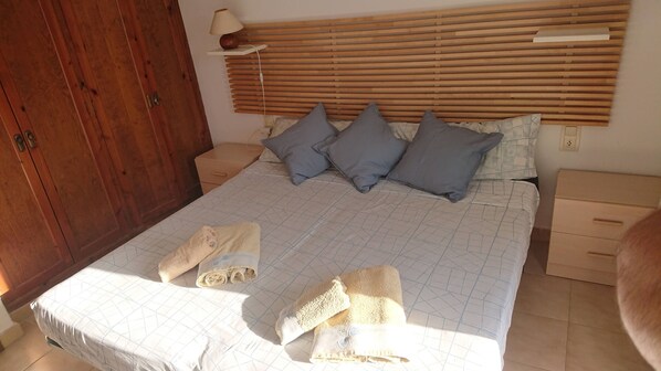 A bedroom with a bed, pillows, a nightstand, a lamp, and a wooden wardrobe.