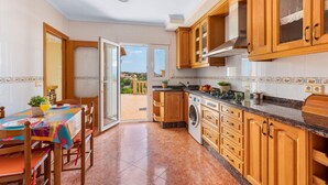 Cozinha compacta com armários de madeira, máquina de lavar e área de refeições com mesa e cadeiras.