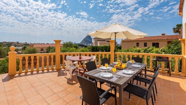 Terraço com mesa posta para refeições, área de estar externa e vista para a paisagem urbana.