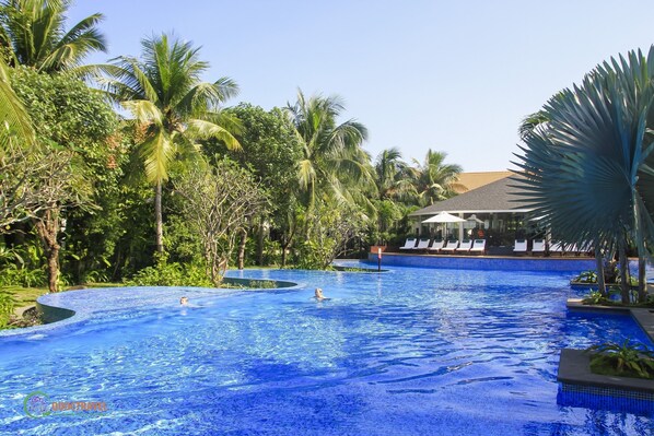Relax by the serene pool surrounded by lush tropical vegetation and palm trees.
