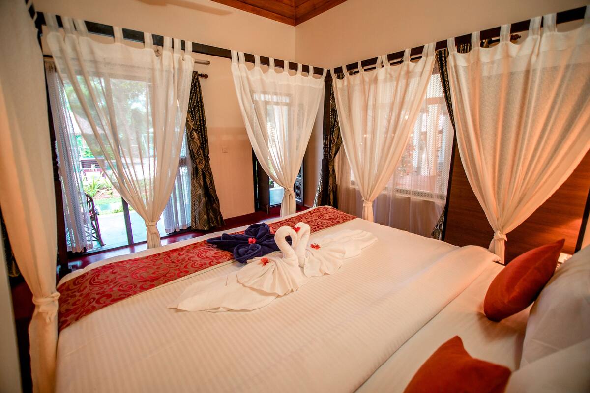 Een hotelkamer met een groot bed, witte gordijnen en een rode sprei.