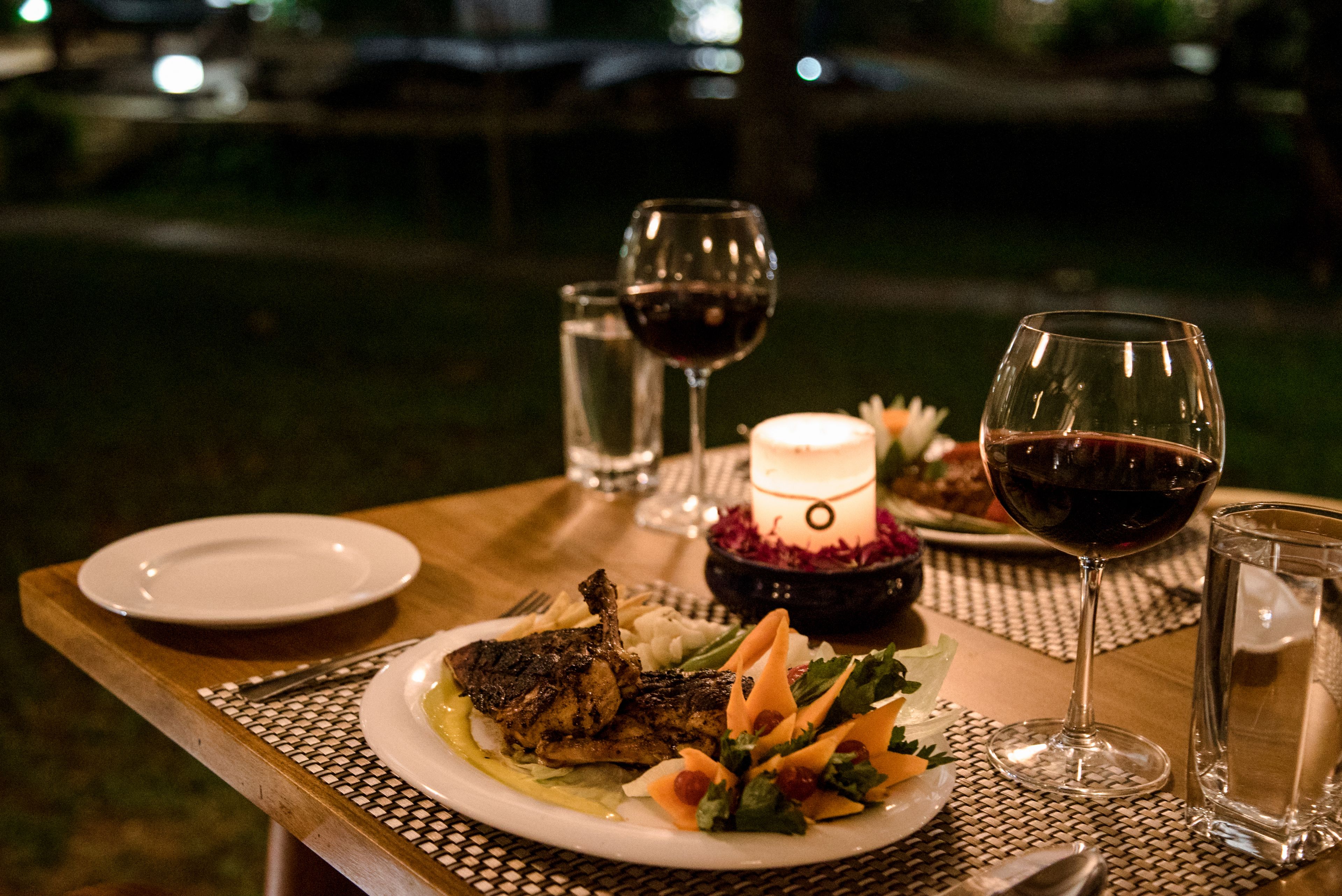 Una mesa de comedor dispuesta con platos, cubiertos y copas de vino tinto, junto con una vela y un adorno decorativo.