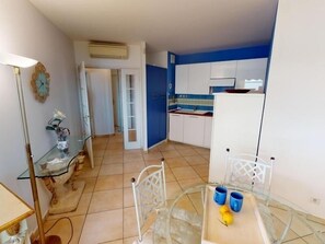Une cuisine compacte avec des meubles blancs, un mur d’accent bleu et une table à manger en verre, agrémentée de deux tasses bleues et d’un citron.