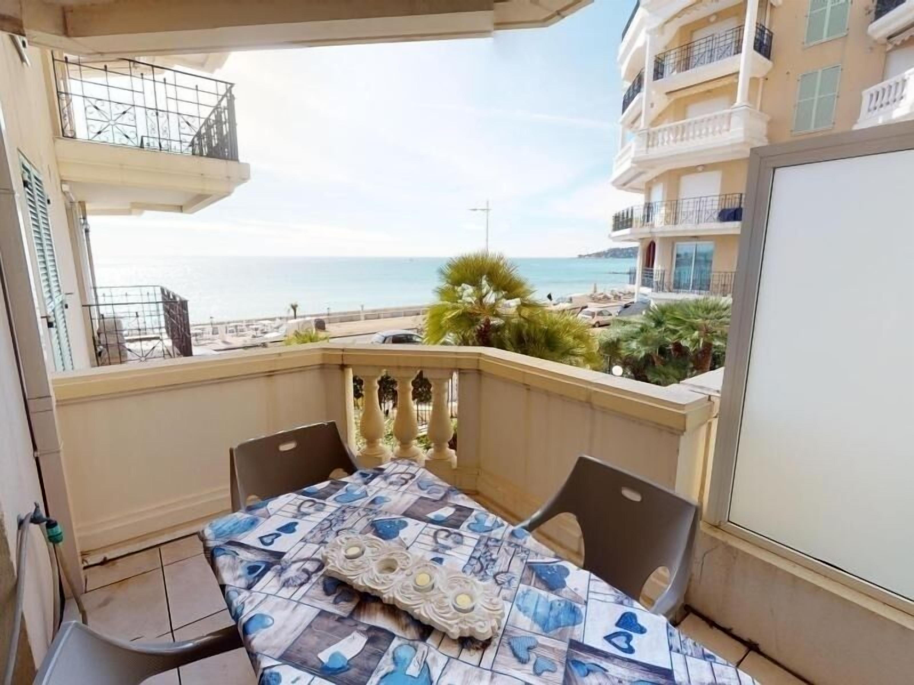 A balcony with a table and chairs, overlooking a beach and a building with balconies.