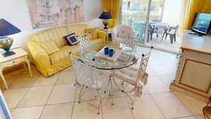 Un soggiorno con un divano giallo, un tavolo da pranzo in vetro e sedie, una televisione e un quadro appeso al muro.