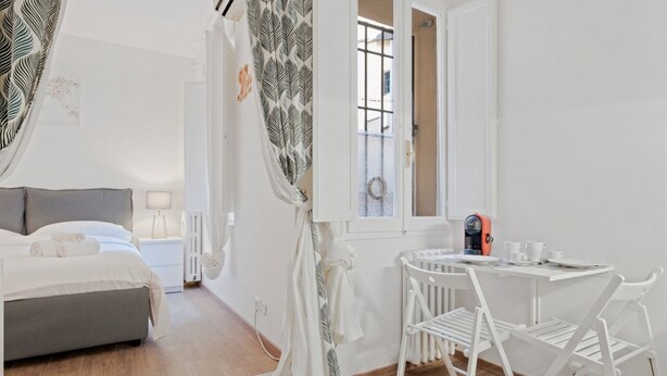 Ein Schlafzimmer mit Bett, Nachttisch, Lampe und Blick ins Freie durch ein Fenster.