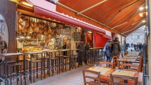 Ein Straßencafé mit Tischen und Stühlen, ein rotes Markisenvorzelt und ein Blick auf ein Gebäude im Hintergrund.