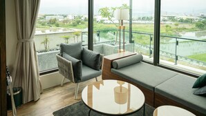A modern living room with a sofa, armchairs, a small round table, and a view of a river and greenery. - Tsang Kuo Resort (Wujie)