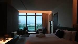A hotel room with a large bed, a small table, two chairs, a TV, and a view of the city through large windows. - Tsang Kuo Resort (Wujie)