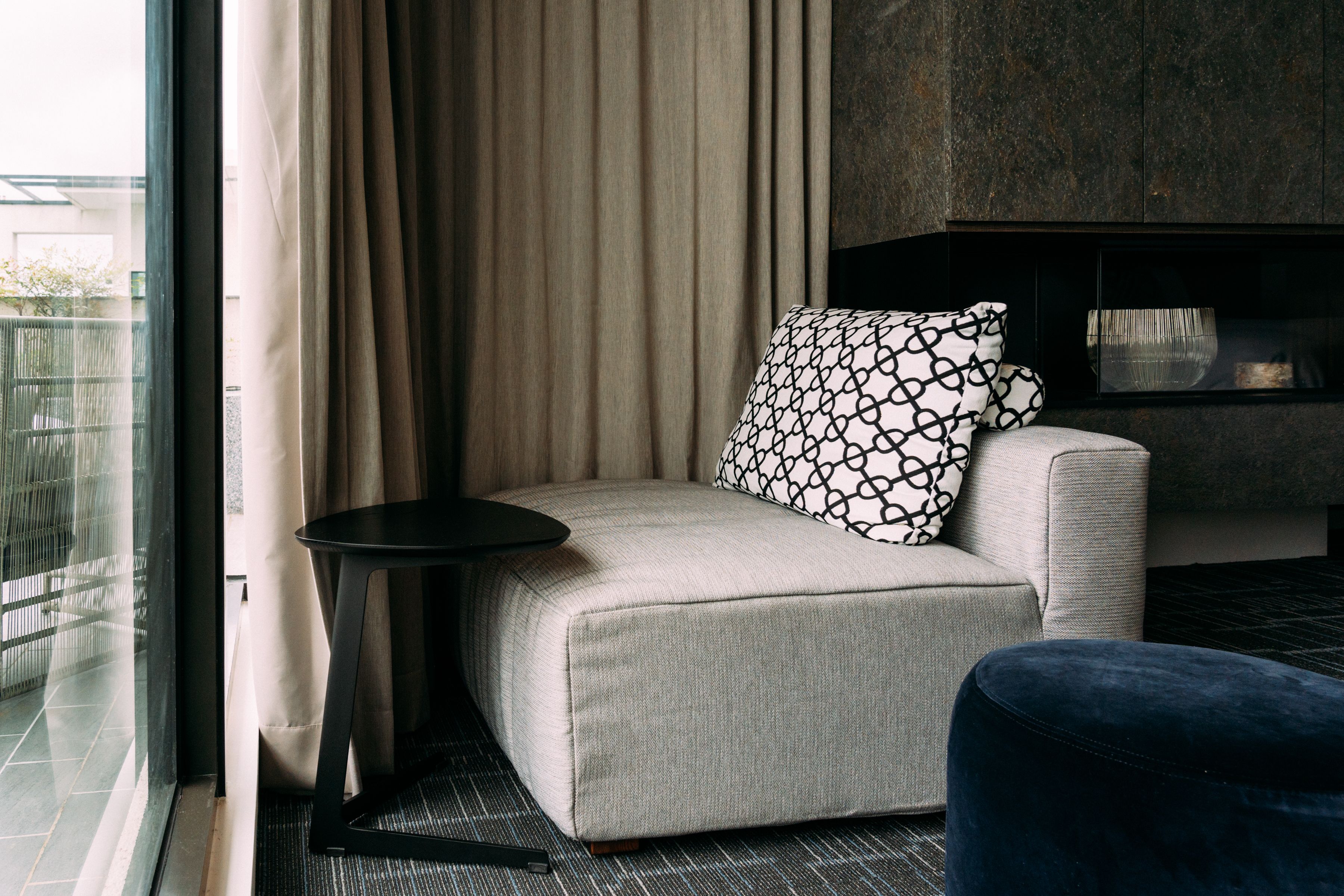 A modern hotel room with a sofa, a small round table, and a view of the outdoors.