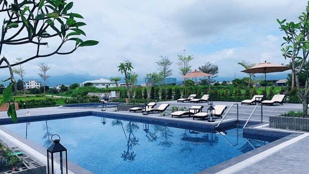 A rectangular swimming pool with lounge chairs and umbrellas, surrounded by greenery and a view of distant buildings. - Tsang Kuo Resort (Wujie)